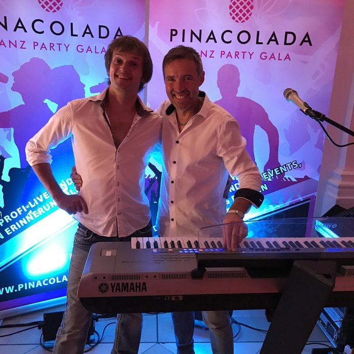 Zwei Musiker von Pina Colada am Keyboard vor dem Bandbanner